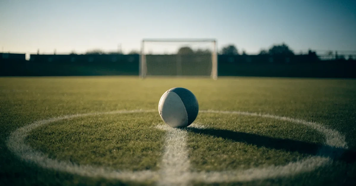 Un pallone da calcio sul dischetto del centrocampo di un prato, alla luce del mattino