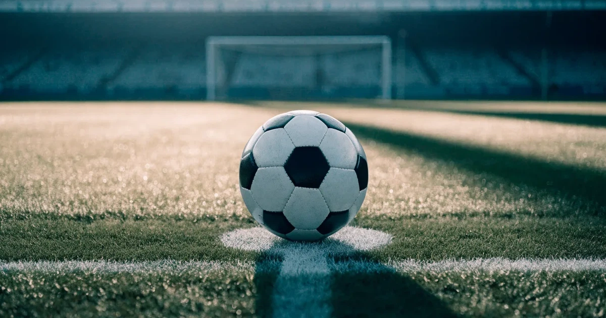Un pallone da calcio sul dischetto del centrocampo di un prato, alla luce del mattino
